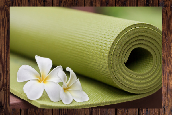 Close up of a green yoga mat with two white flowers in the foreground and wood pattern border.